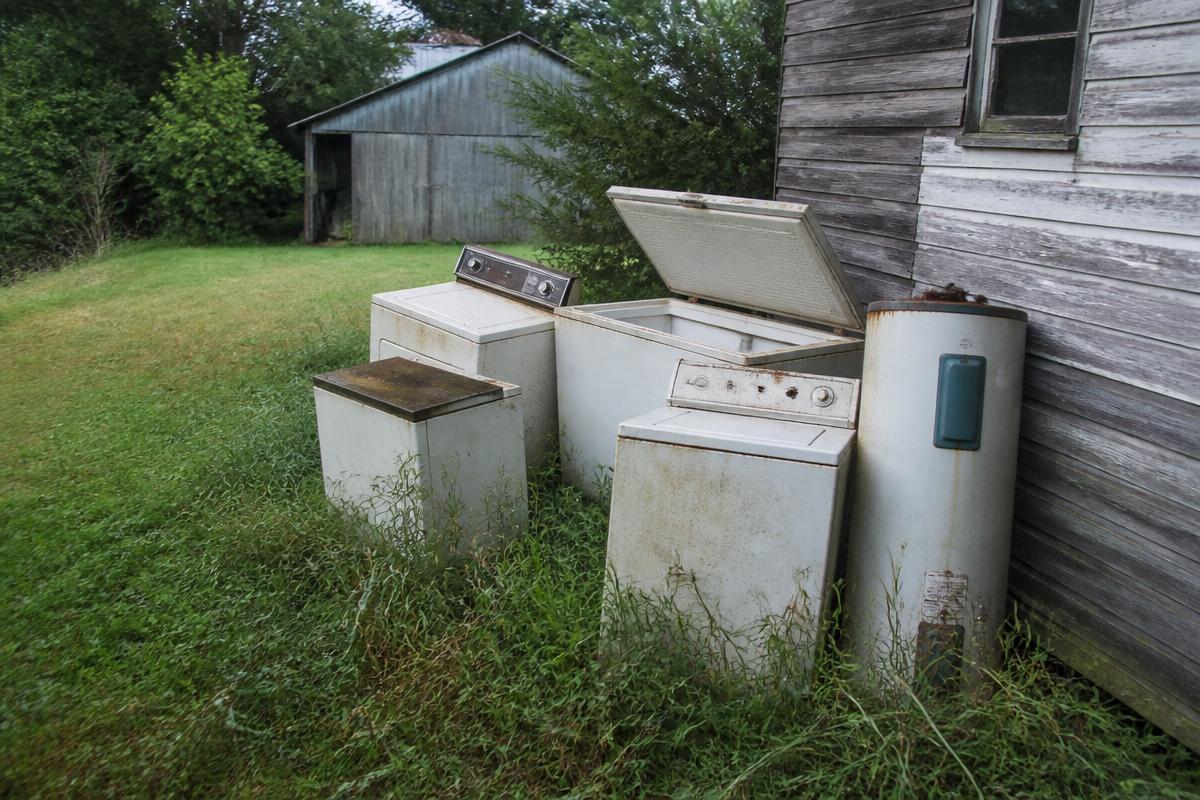 Pile of rusted appliances beside a farmhouse before removal in Lawndale, NC